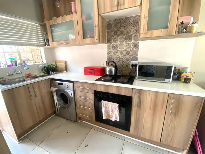 Functional kitchen featuring wood-look cabinetry, laminate countertops, built-in oven and hob, tiled splashback, and integrated space for a washing machine.
