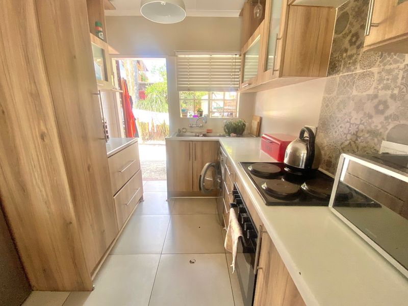 Compact galley-style kitchen featuring wood-look cabinetry, electric hob, built-in oven, patterned backsplash, and direct access to the rear exterior.
