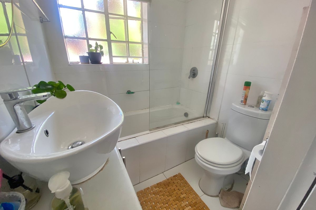A functional bathroom featuring a vessel sink, a built-in bathtub with a glass shower screen, and a standard toilet with tiled finishes.