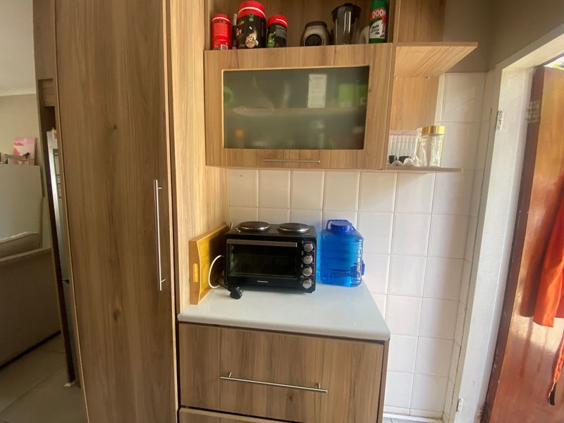 A compact scullery or prep area featuring wood-look built-in cabinetry, laminate countertops, and a tiled backsplash.