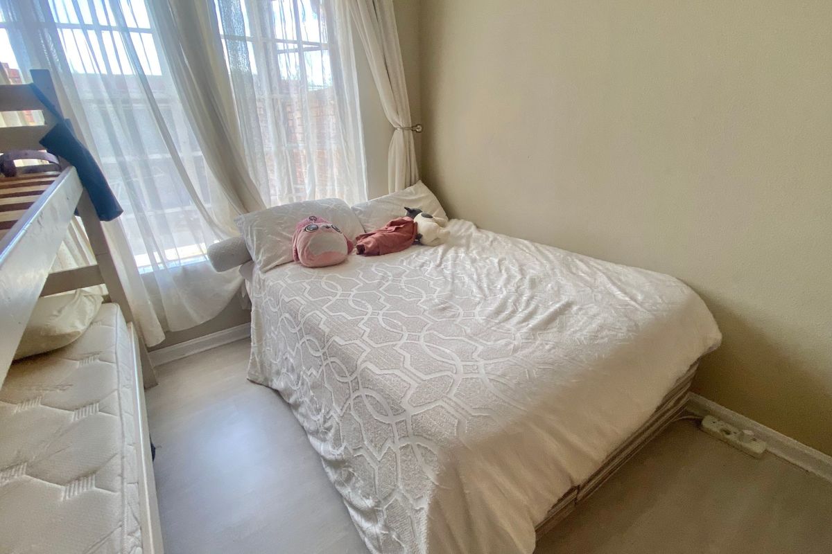 A compact bedroom featuring light-toned laminate flooring and large windows with installed curtain tracks, providing natural light to the space.