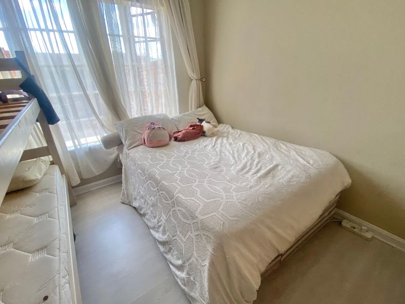 A compact bedroom featuring light-toned laminate flooring and large windows with installed curtain tracks, providing natural light to the space.