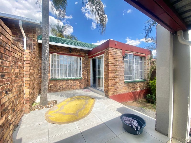 A rear exterior view of a face brick townhouse featuring a tiled patio area and sliding glass door access.
