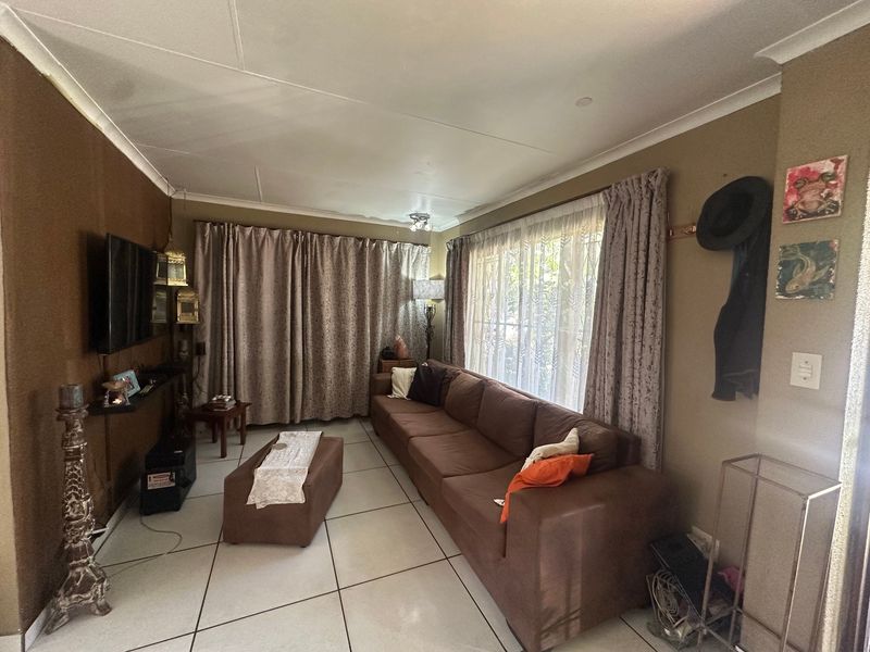 A living room featuring tiled flooring and large windows with curtains, offering a functional space with potential for modern updates.