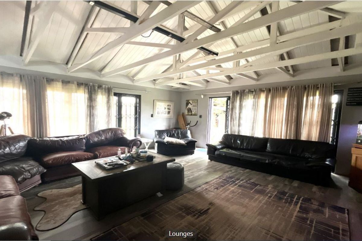 Spacious living room featuring a high vaulted ceiling with exposed white timber rafters, laminate flooring, and multiple access points to the exterior.