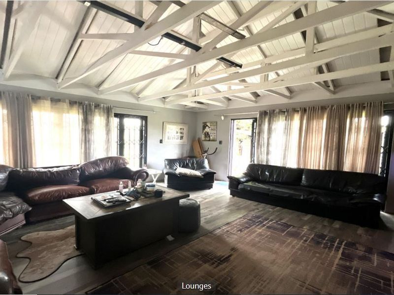 Spacious living room featuring a high vaulted ceiling with exposed white timber rafters, laminate flooring, and multiple access points to the exterior.