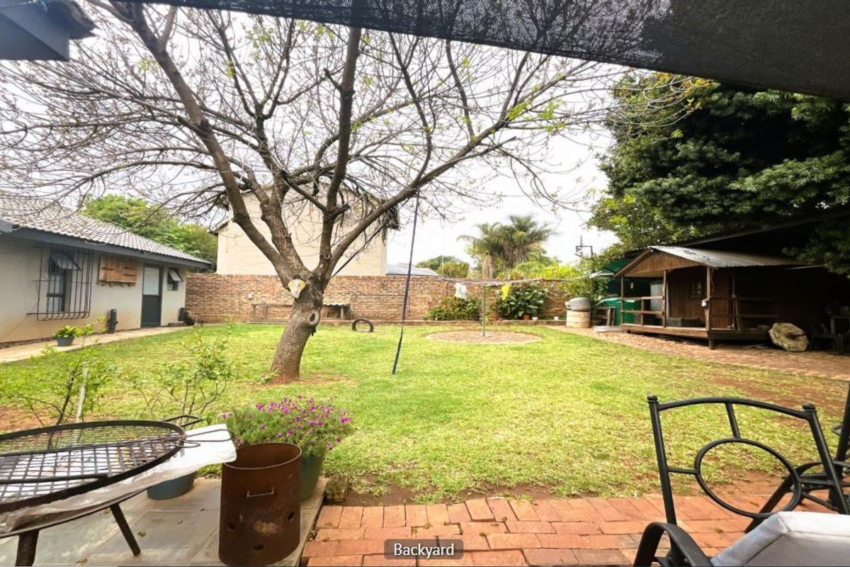 A spacious rear garden featuring a paved patio area, established lawn, mature tree, and brick boundary wall, providing a private outdoor space.