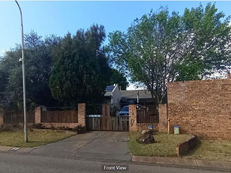 Front view of the property featuring a brick boundary wall, gated driveway entrance, and a tiled roof house with solar panels.