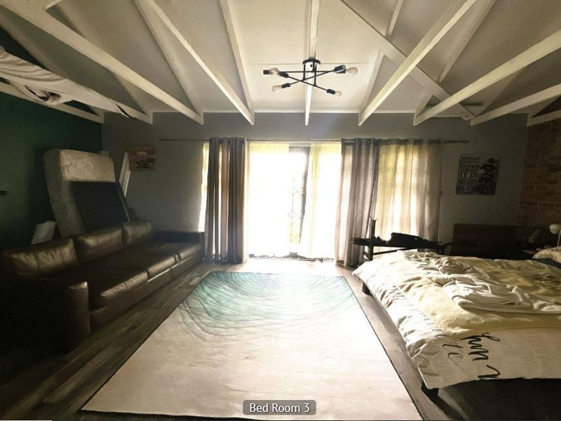Spacious bedroom featuring exposed timber rafters, an exposed brick feature wall, and sliding glass doors providing natural light.