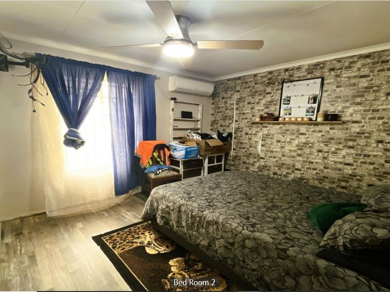 A bedroom featuring a brick-effect accent wall, laminate flooring, a ceiling fan, and a wall-mounted air conditioning unit.