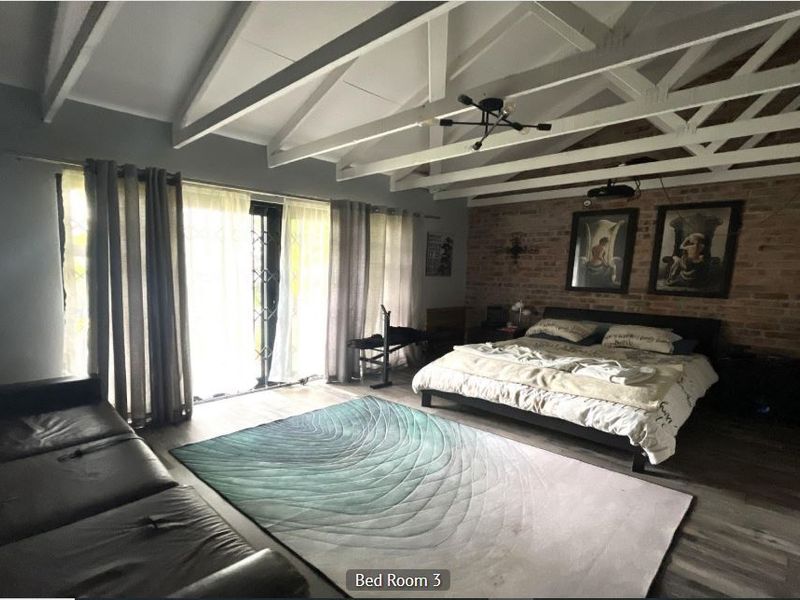 Spacious bedroom featuring exposed timber rafters, a rustic brick feature wall, and sliding glass doors providing access to the exterior.
