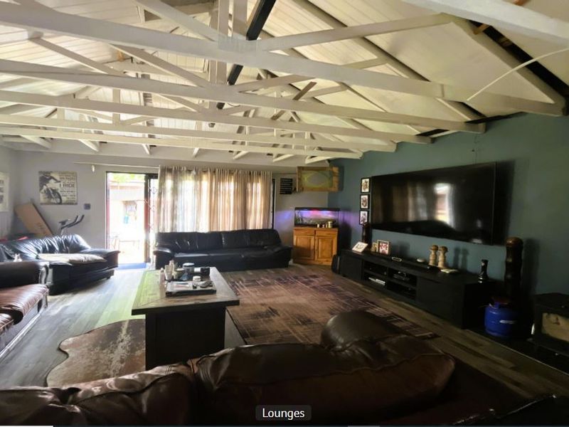 Spacious living room featuring exposed white timber roof trusses, a wood-burning fireplace, and laminate flooring with access to the outdoor area.