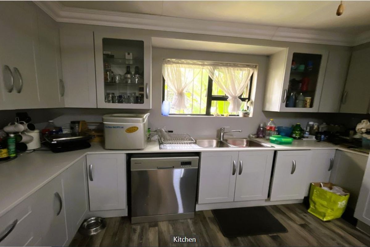 A functional kitchen featuring light-toned cabinetry, a double bowl sink, and integrated dishwasher, finished with modern laminate flooring and decorative coving.