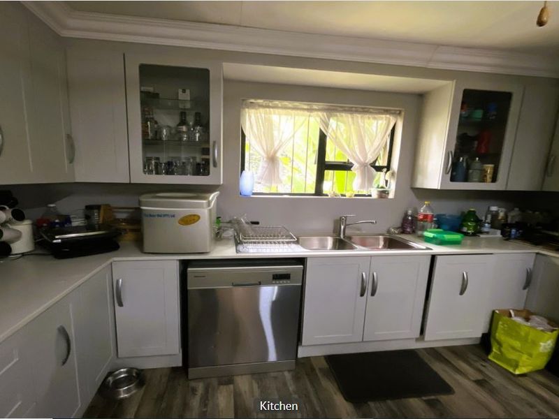 A functional kitchen featuring light-toned cabinetry, a double bowl sink, and integrated dishwasher, finished with modern laminate flooring and decorative coving.