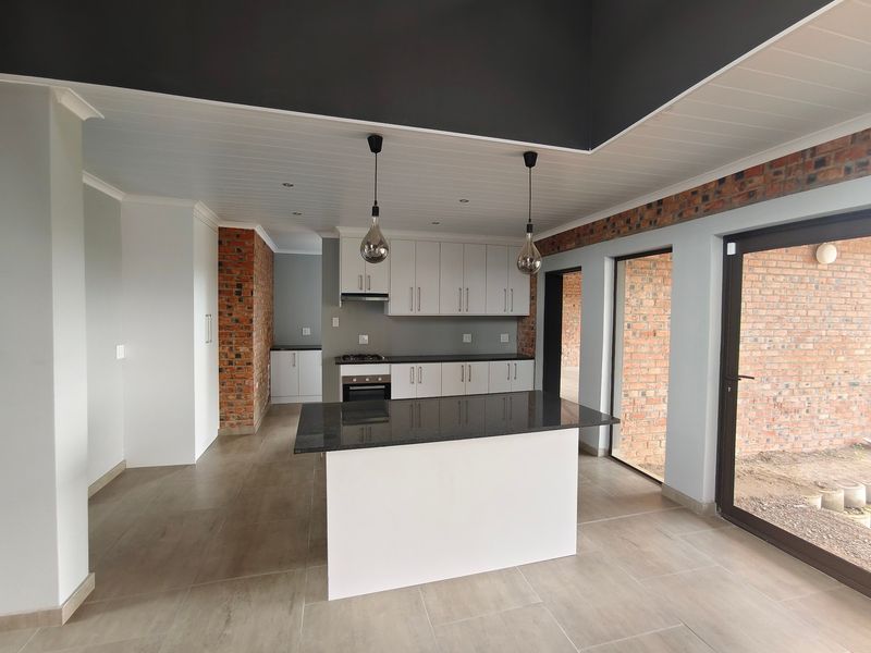 Modern open-plan kitchen featuring a central island, granite countertops, built-in appliances, and stylish exposed brick accents with direct access to the outdoor area.