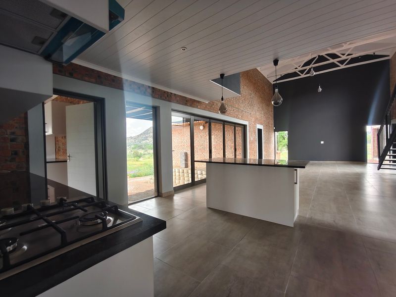 Spacious open-plan living area featuring a modern kitchen with gas hob, island, exposed brick walls, and large sliding doors leading to the exterior.