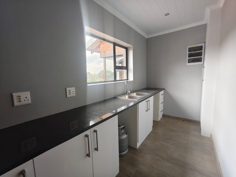 A clean and modern scullery featuring granite countertops, double stainless steel sink, and ample built-in cabinetry with neutral finishes.