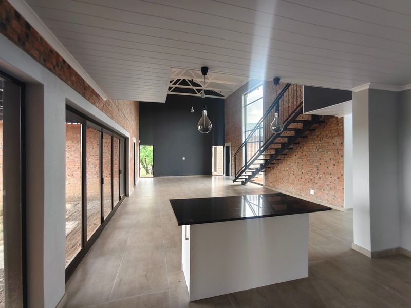 Spacious open-plan living area featuring exposed brick walls, a modern metal staircase, vaulted ceilings, and a central kitchen island with granite countertops.