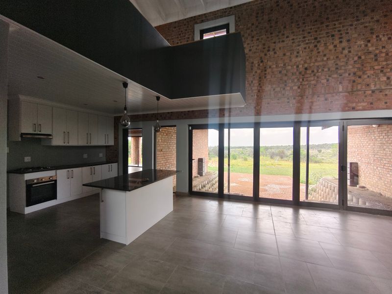 Spacious open-plan kitchen and living area featuring exposed brick walls, modern cabinetry, a central island, and large sliding doors opening to a scenic landscape.