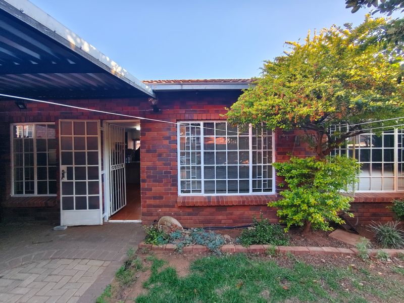 Rear view of the townhouse featuring a face brick facade, covered patio area, and secure entrance with security gate and bars.