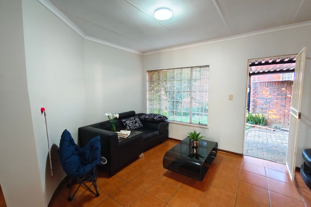 A living room featuring tiled flooring, coved ceilings, and direct access to an outdoor patio area through a security gate.