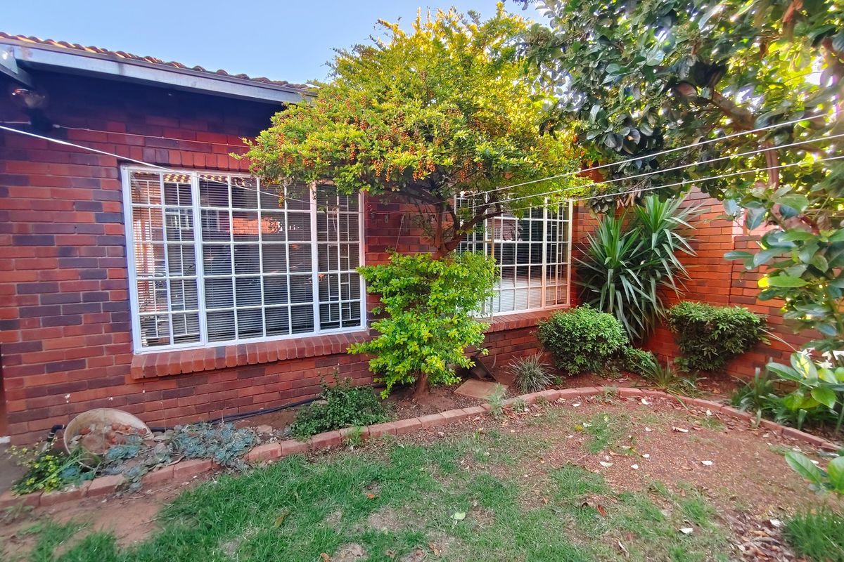 A view of the rear face brick facade of the townhouse, featuring security-barred windows and a small garden area with established trees.