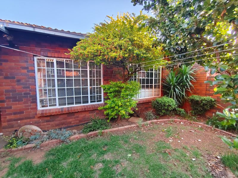 A view of the rear face brick facade of the townhouse, featuring security-barred windows and a small garden area with established trees.