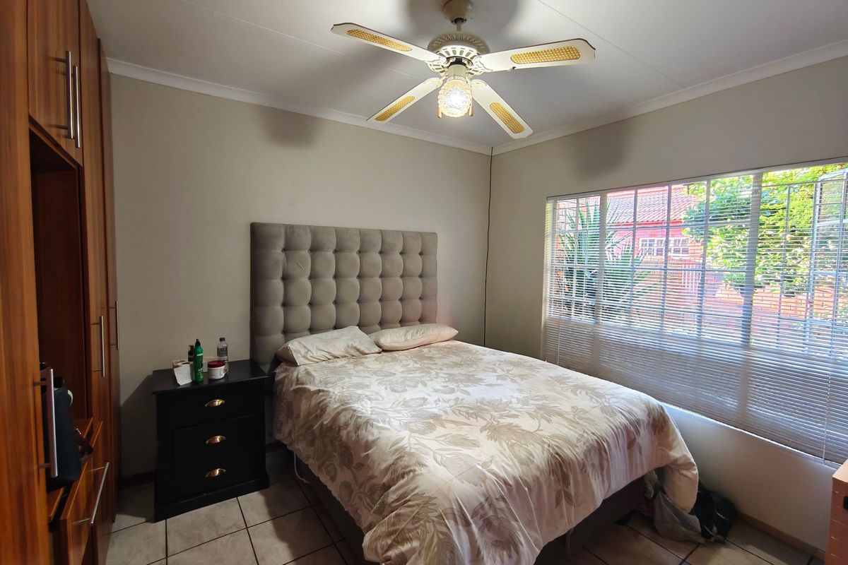 A functional bedroom featuring built-in cupboards, tiled flooring, a ceiling fan, and venetian blinds, offering a comfortable and practical living space.