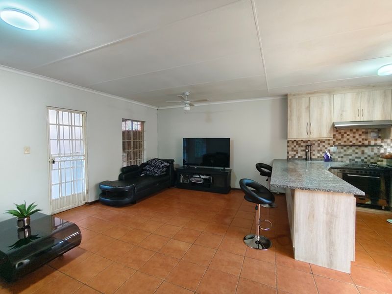 Open-plan living area featuring tiled flooring, a functional kitchen with granite countertops, and direct access to the exterior via a security gate.