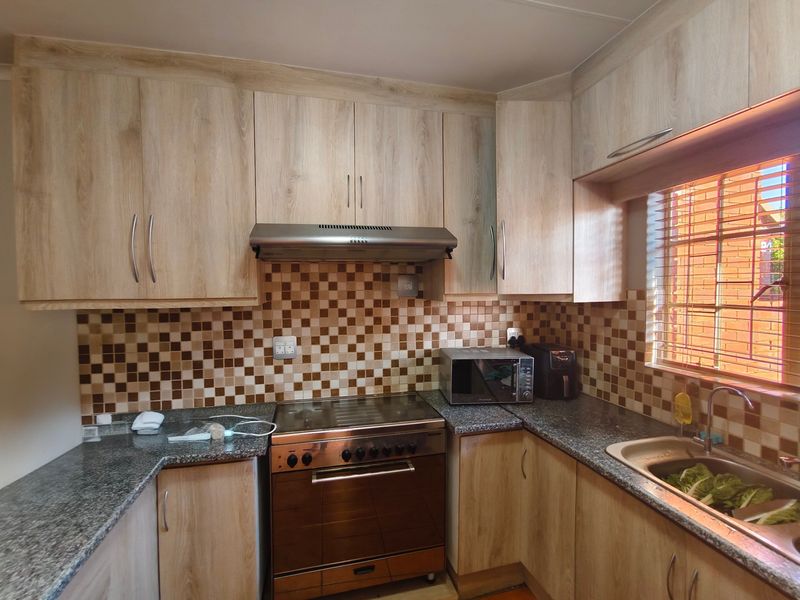 A functional kitchen featuring light wood-look cabinetry, granite countertops, a mosaic tile backsplash, and a stainless steel stove with an extractor fan.