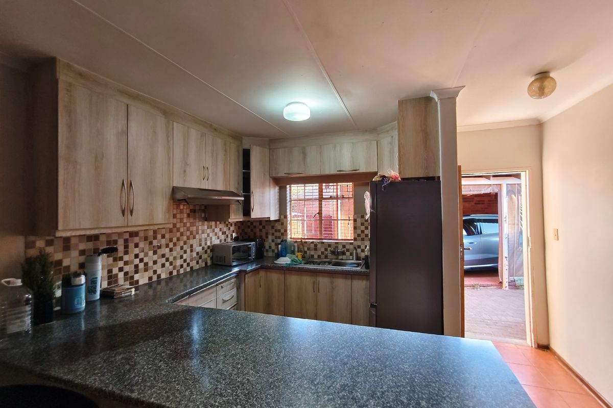 Functional kitchen featuring laminate cabinetry, granite countertops, mosaic tile backsplash, and a stainless steel extractor fan, with direct access to the exterior.