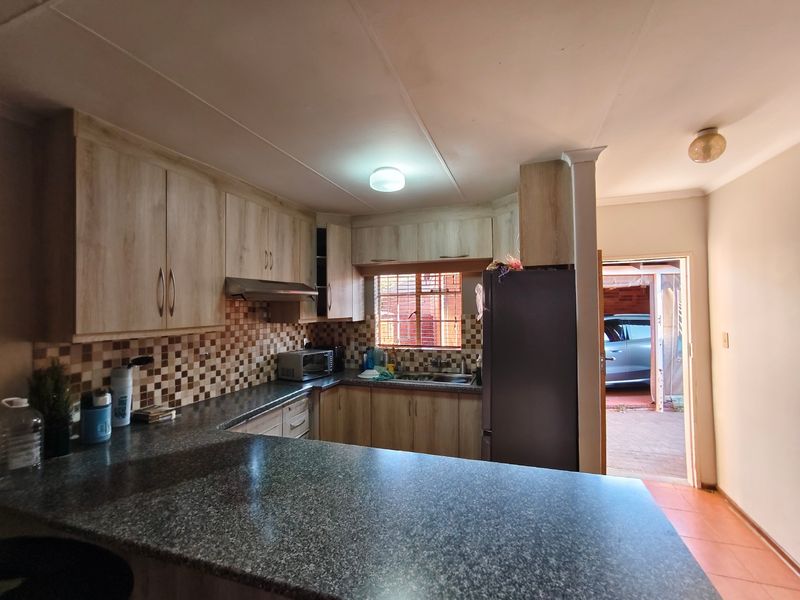 Functional kitchen featuring laminate cabinetry, granite countertops, mosaic tile backsplash, and a stainless steel extractor fan, with direct access to the exterior.