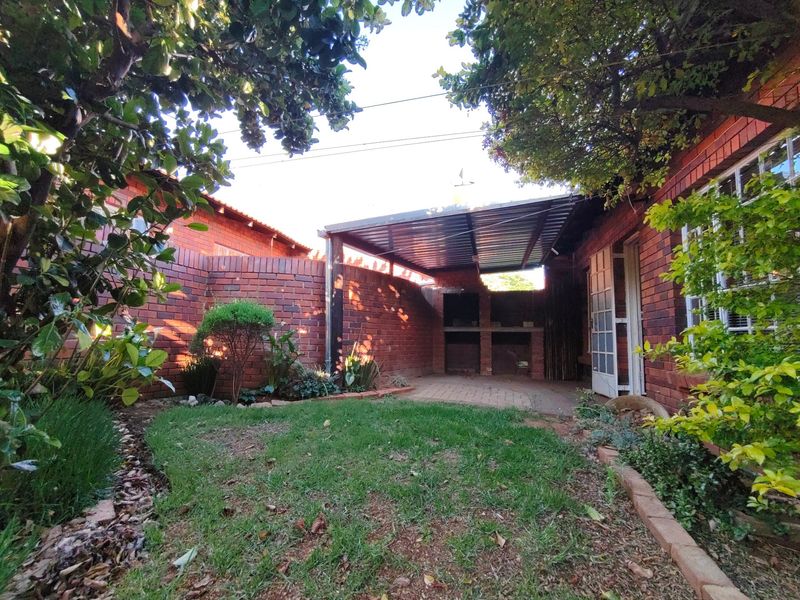 A private rear garden featuring a brick-walled courtyard, a covered patio area with a built-in braai, and a small lawn.