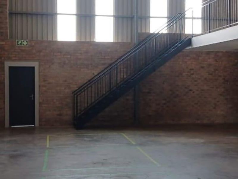 Spacious industrial utility area featuring exposed brick walls, a metal staircase leading to a mezzanine level, and durable concrete flooring.