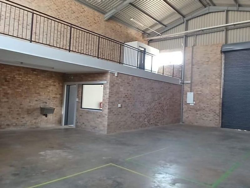 Spacious industrial utility area featuring exposed brick walls, a mezzanine level with steel balustrades, concrete flooring, and a large roller shutter door.