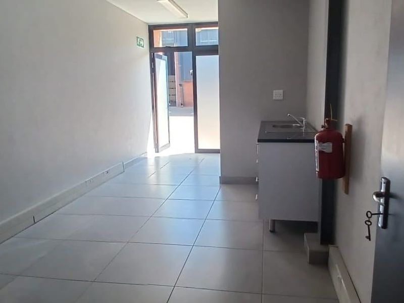 A clean, functional utility space featuring tiled flooring, a compact kitchenette cabinet with a sink, and direct access to the exterior.