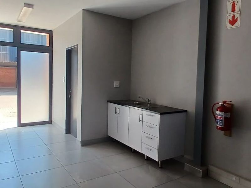 A clean, functional utility space featuring tiled flooring, a built-in kitchenette unit with a sink, and direct access to the exterior.