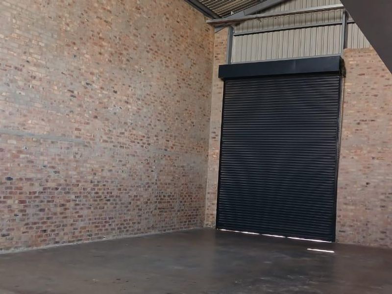 Spacious industrial utility area featuring exposed brick walls, polished concrete flooring, and a large roller shutter door for easy access.
