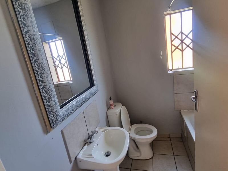 A compact bathroom featuring a pedestal basin, toilet, and bathtub with tiled flooring and security bars on the window.