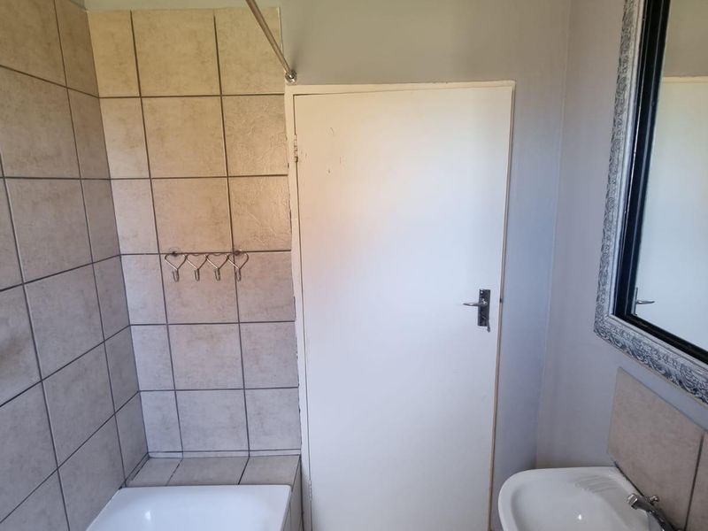 A functional bathroom featuring a bathtub with tiled surround, pedestal basin, and neutral wall finishes, offering a clean and practical space.