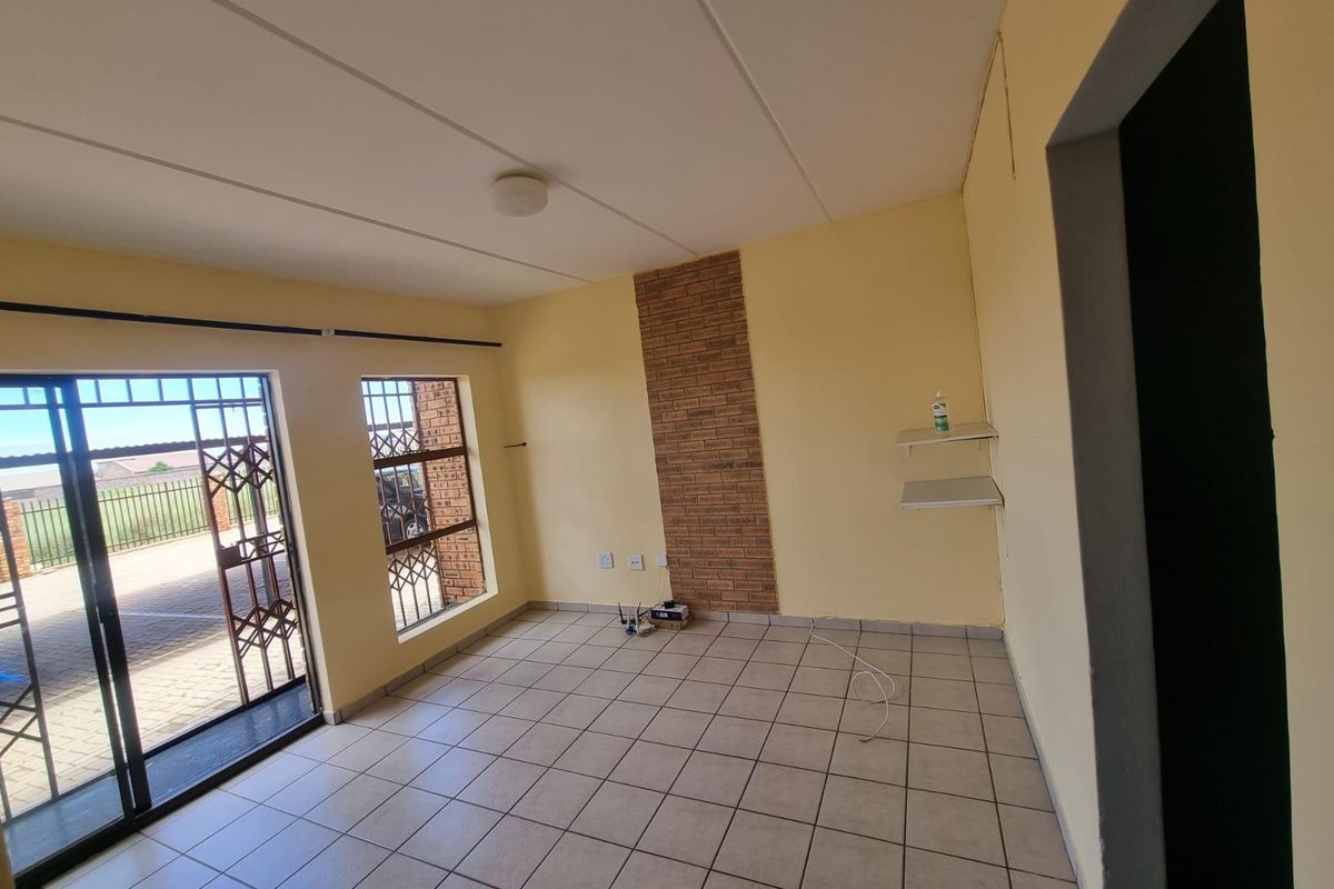 An empty living room featuring ceramic floor tiles, a brick feature wall, and a sliding glass door with security gate access to the exterior.
