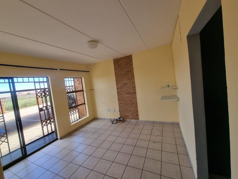 An empty living room featuring ceramic floor tiles, a brick feature wall, and a sliding glass door with security gate access to the exterior.