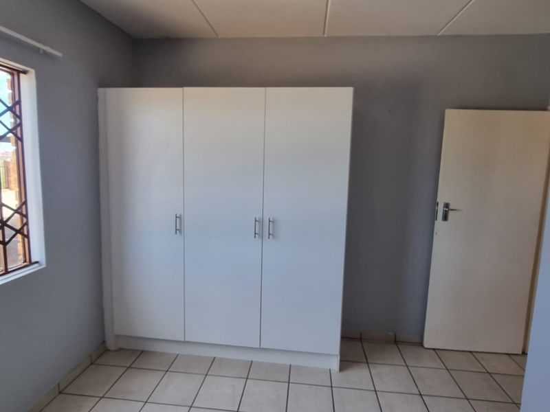 A clean, empty bedroom featuring neutral grey walls, white built-in wardrobes, and tiled flooring with a security-fitted window.