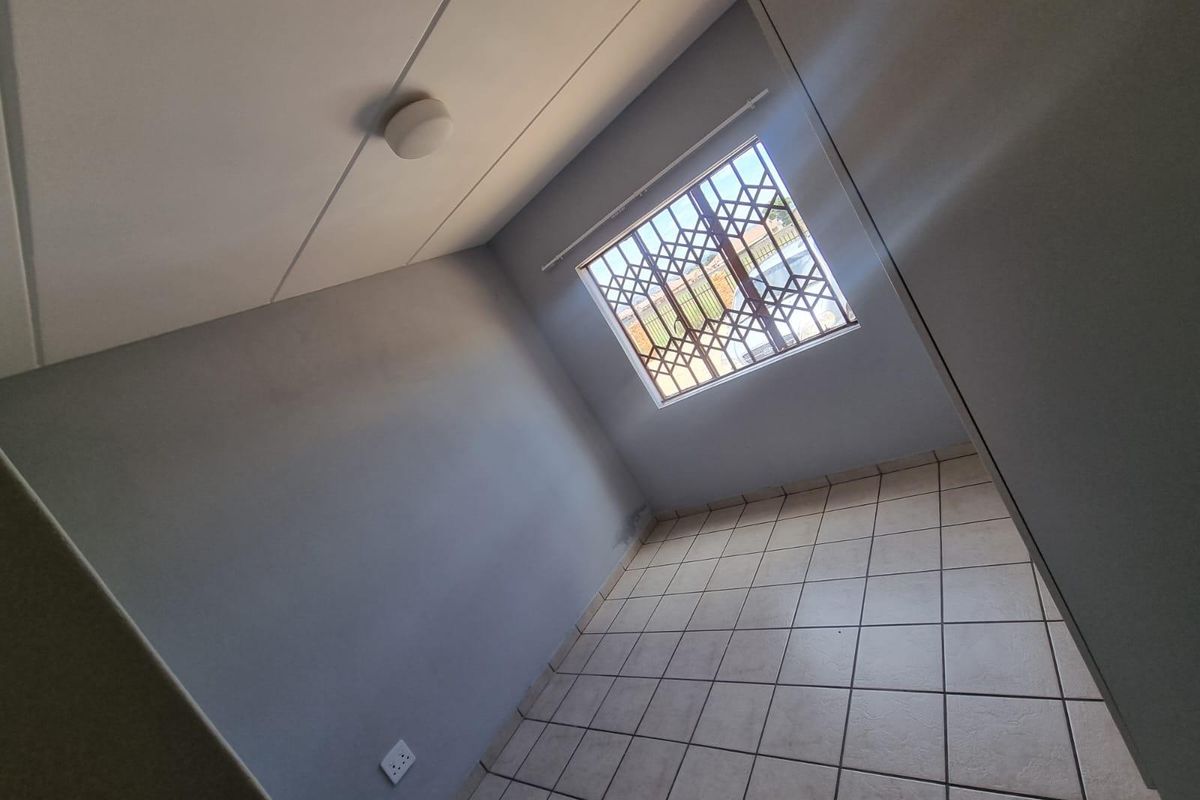 An empty bedroom featuring tiled flooring, a window with a security gate, and neutral wall finishes.