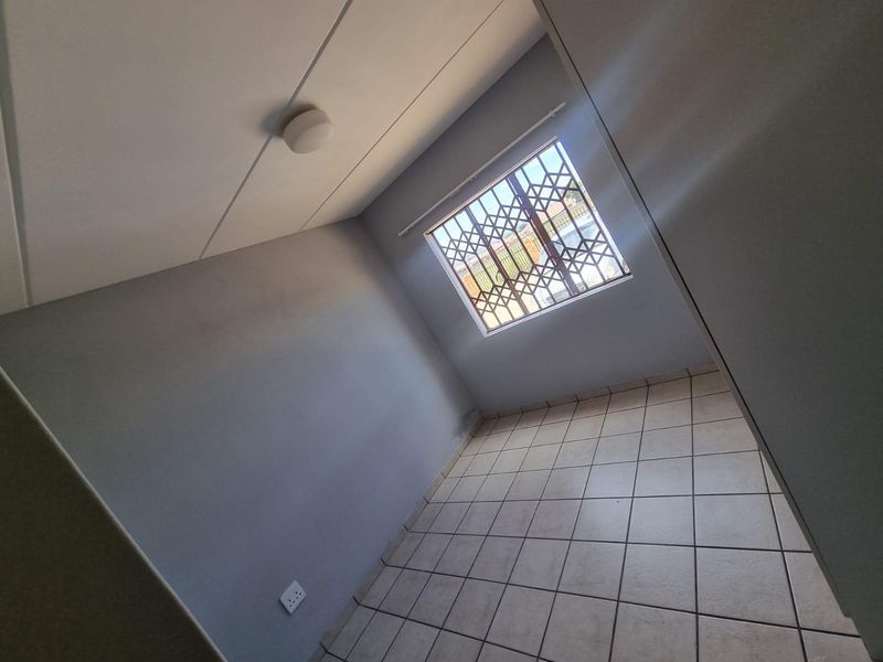 An empty bedroom featuring tiled flooring, a window with a security gate, and neutral wall finishes.