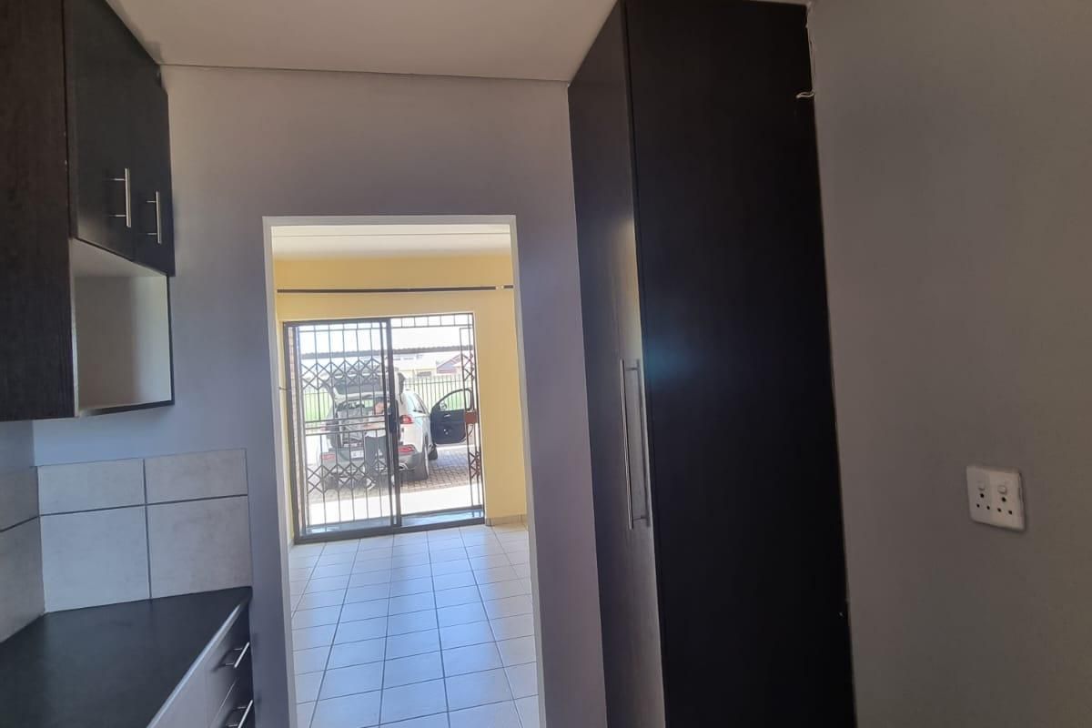 A functional kitchen area featuring dark built-in cabinetry, tiled flooring, and a tall pantry cupboard, leading through to an exterior access point.