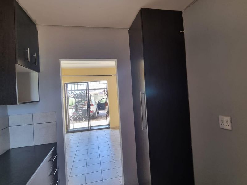 A functional kitchen area featuring dark built-in cabinetry, tiled flooring, and a tall pantry cupboard, leading through to an exterior access point.
