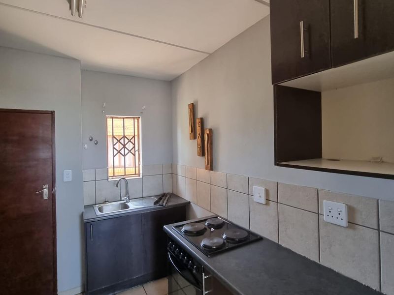 A functional kitchen featuring dark built-in cabinetry, a tiled backsplash, integrated oven and hob, and tiled flooring.