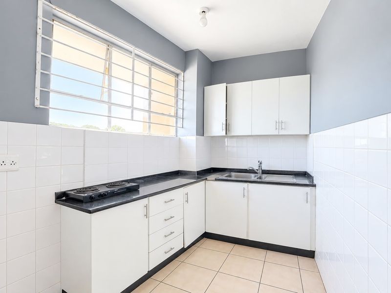 A clean, functional kitchen featuring white cabinetry, dark countertops, an electric hob, and tiled finishes, offering a bright and well-maintained workspace.