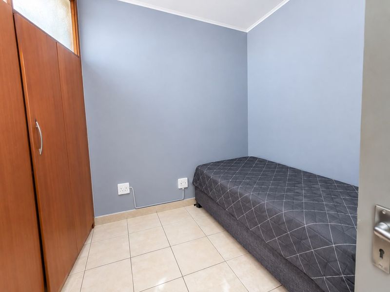 A compact bedroom featuring neutral grey walls, tiled flooring, and a built-in wooden wardrobe.